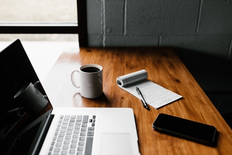 business desk with coffee cup, laptop, notepad, and cellphone