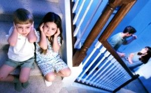 two children sitting at the top of the stairs with ears plugged while their parents fight downstairs